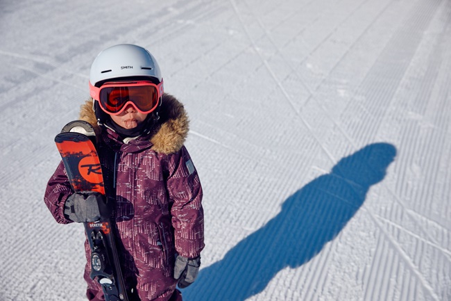 Une petite skieuse avec un casque fait une grimace en tenant ses skis