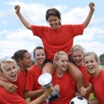 Portrait of an all-girls soccer team raising their captain in triumph