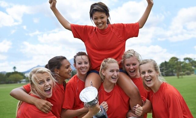 Portrait of an all-girls soccer team raising their captain in triumph