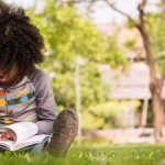 Un petit garçon écrivant sur un cahier assis sur l'herbe verte dans un parc