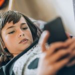 adolescent couché sur le divan qui regarde son téléphone cellulaire