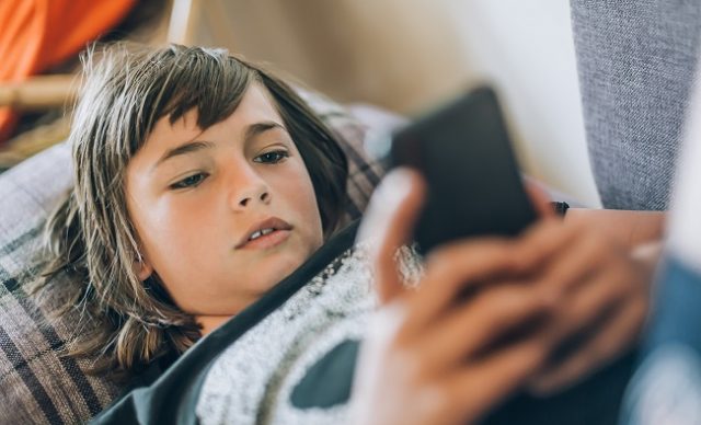adolescent couché sur le divan qui regarde son téléphone cellulaire